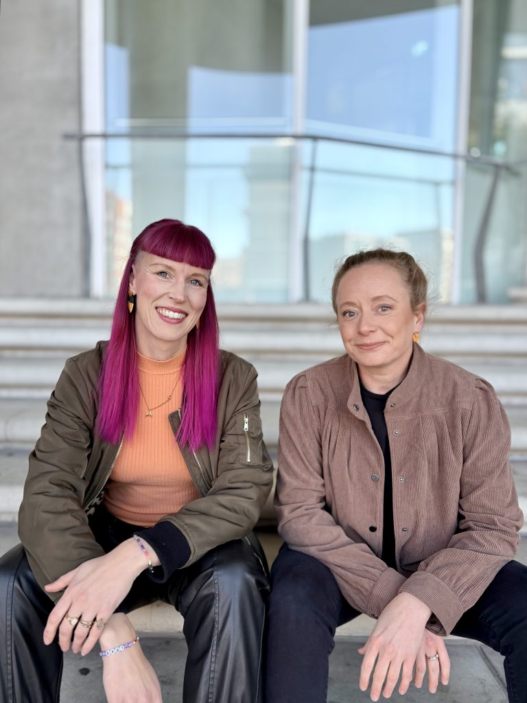Zwei Frauen sitzend auf einer Treppe. Lächeln in die Kamera